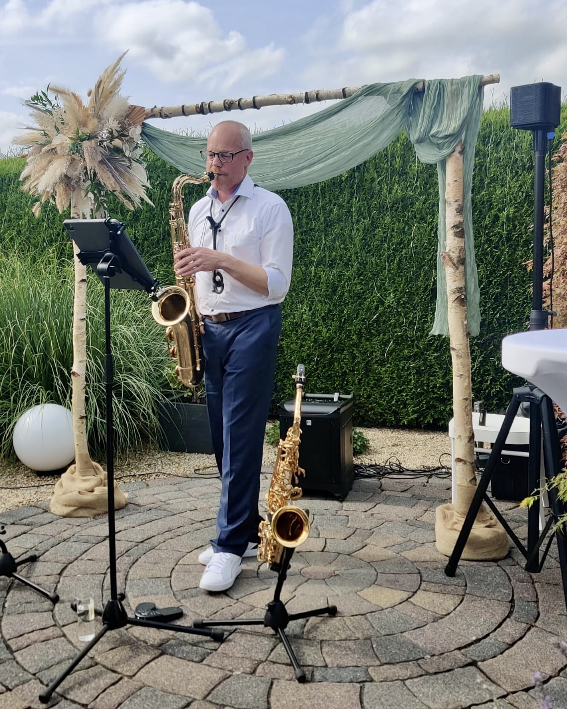 Peter Macherey spielt Tenorsaxophon bei einer Hochzeitsfeier im Garten unter einem geschmückten Traubogen